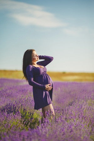 Image of pregnant woman holding her belly, standing in a lavender field.